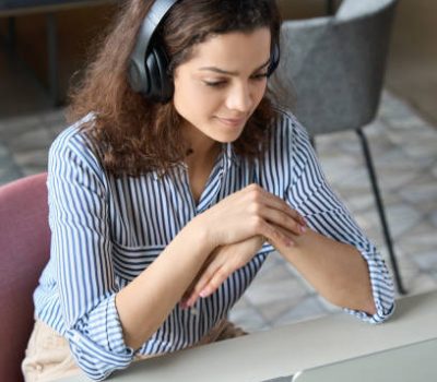 Hispanic girl college student wearing headphones watching distance online learning web class, remote university webinar or having talk on laptop video call virtual meeting seminar at home or campus.
